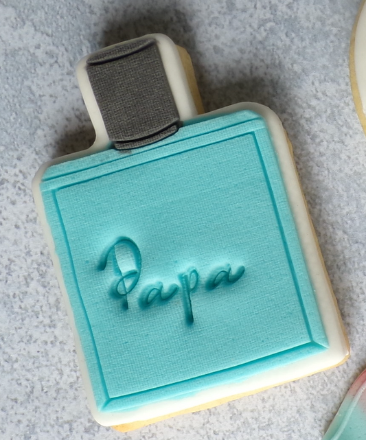 Biscuit sablé décoré en pâte à sucre en forme de parfum avec le bouchon noir et le flacon bleu. Inscription "papa" au milieu