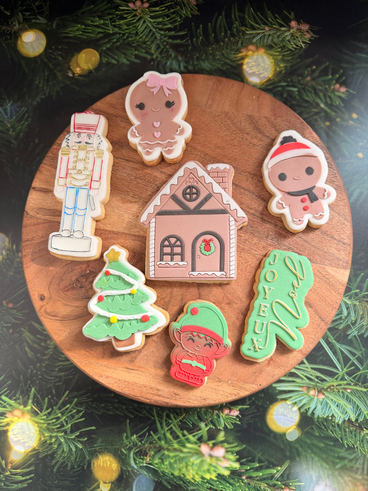 Assortiment de biscuits de Noël décorés artisanalement : bonhomme pain d’épices, maison en pain d’épices, casse-noisette, sapin, lutin et inscription “Joyeux” – Les Folies Gourmandes de Judy.