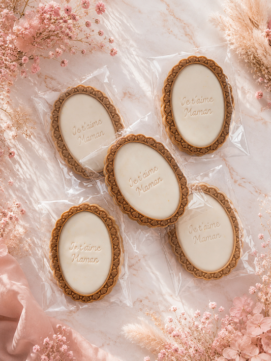 Biscuits artisanaux “Je t’aime Maman” décorés en pâte à sucre ivoire sur fond rose poudré floral spécial Fête des Mères