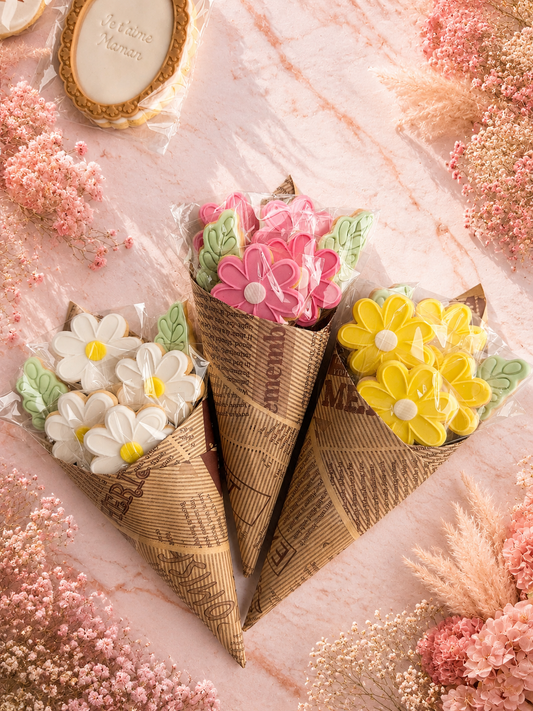 Bouquet de biscuits fleurs décorés en pâte à sucre rose, blanc et jaune avec feuilles vertes dans un emballage kraft spécial Fête des Mères
